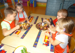 Grupa dzieci miesza łyżkami owoce w misce.